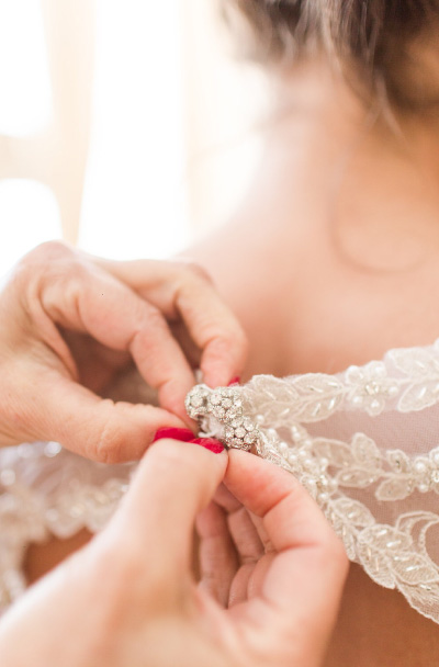 An assistant helps an Emily Weddings bride button her dress