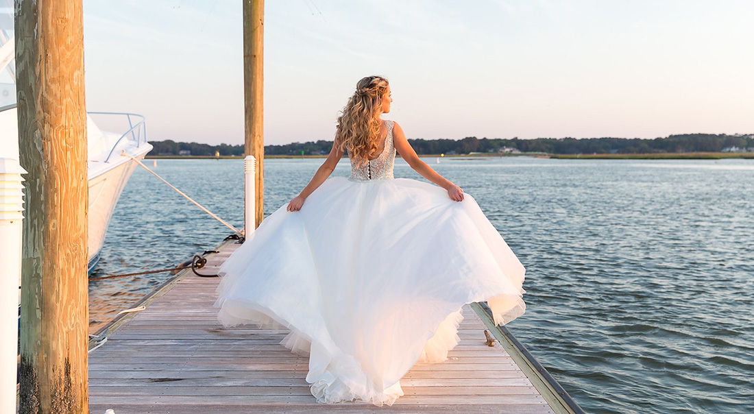 An Emily Weddings' bride's dress flows in the breeze on the dock in Virginia Beach